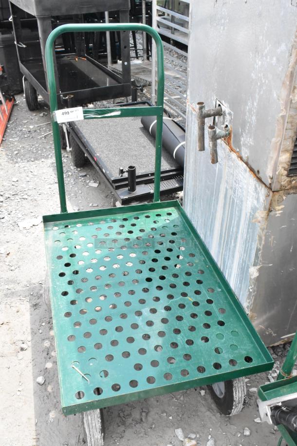 Green metal flat cart with perforated platform, sturdy handle, and wheels. Light wear, ideal for transporting heavy items.