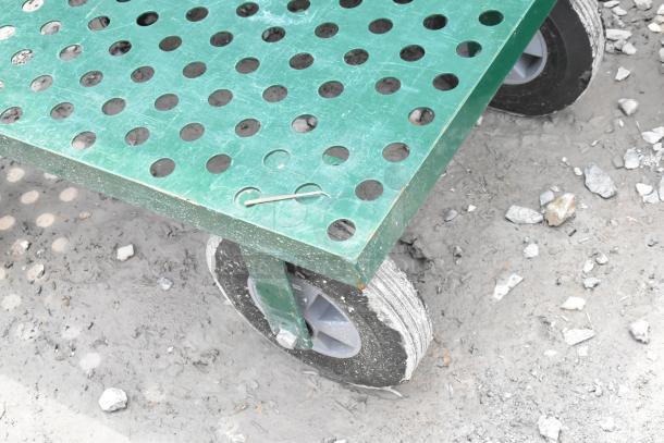 Green metal flat cart with perforated surface, heavy-duty wheels, and visible signs of wear. Suitable for industrial use.