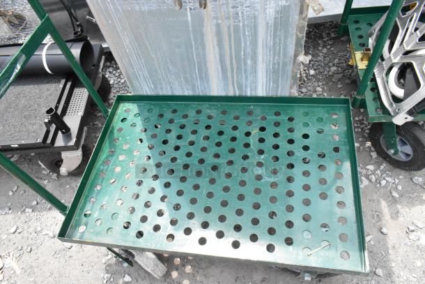 Green metal flat cart with perforated surface, in used condition. Features durable wheels and sturdy frame. Ideal for heavy loads.