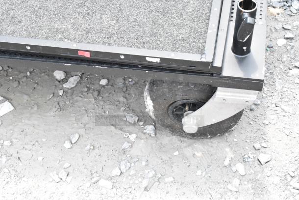 Heavy-duty cart on casters with textured surface, metal frame, and a cup holder. Shows wear on caster wheel, suitable for rugged use.