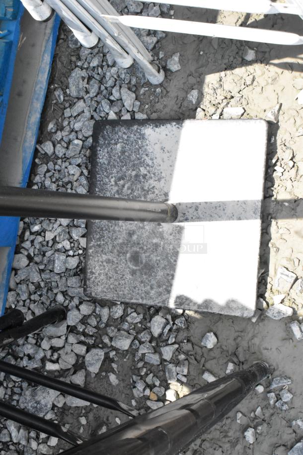 Metal stand on a gravel surface, featuring sturdy black poles and a flat, square base. Appears in used outdoor condition.