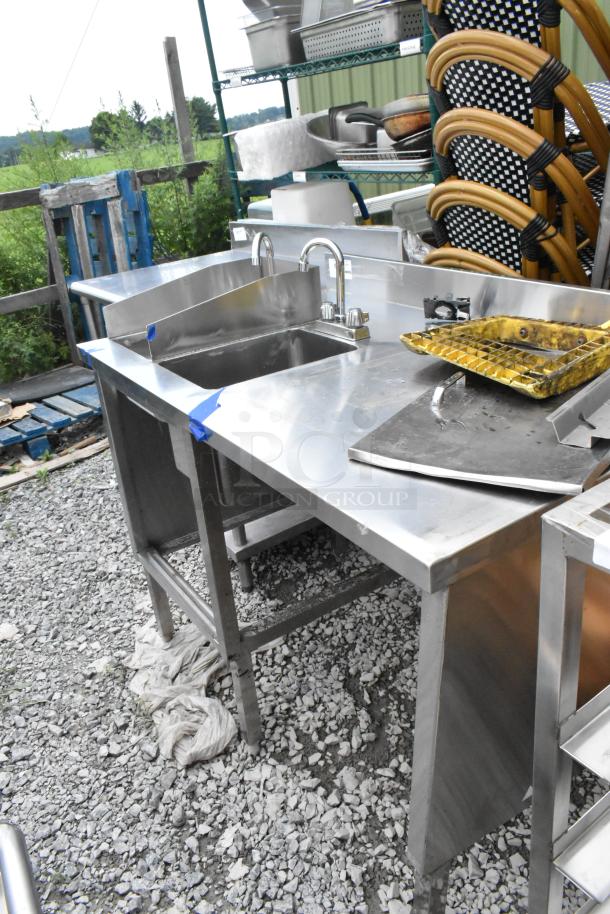Stainless steel table with two single sink bays and faucets, in good condition, visible in a storage area.