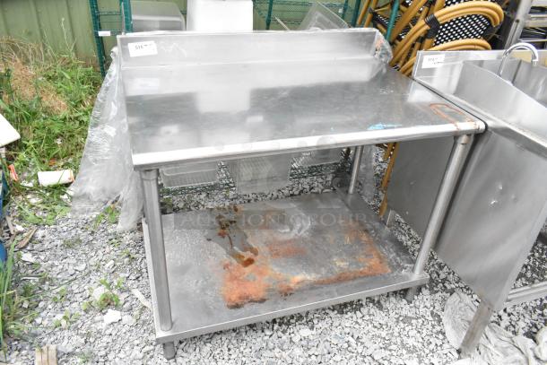 Stainless steel table with under shelf, back splash, visible rust on shelf, tags with lot number, ideal for commercial use.