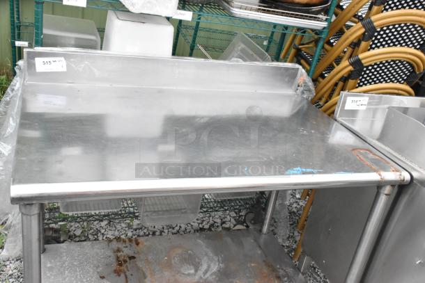 Stainless steel table with under shelf and back splash. Used condition with visible rust and wear. Price tag $515 visible.