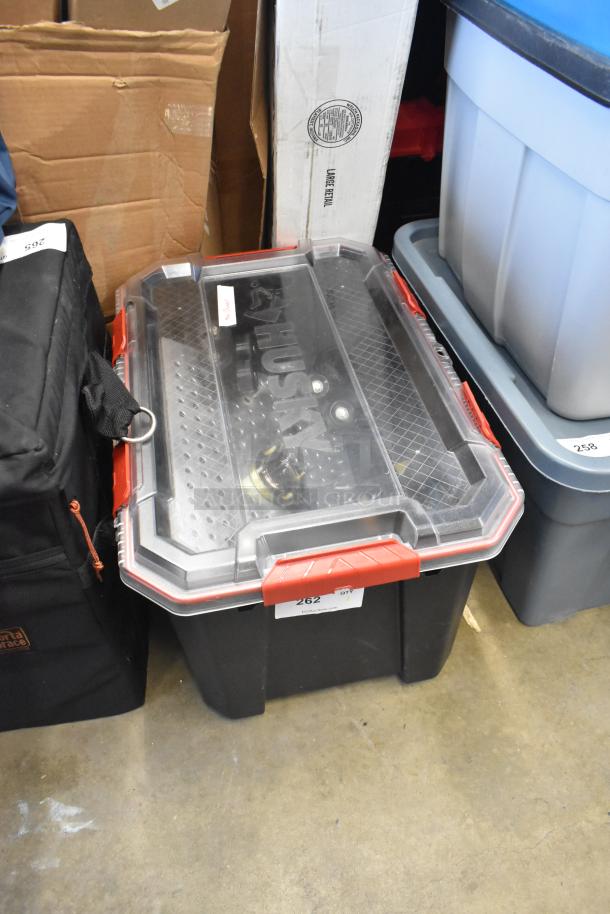 Poly bin with red latches labeled "Husky," containing various items including a Movi Elevator. Visible tag: "262."