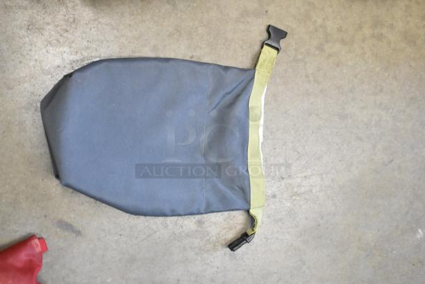 Gray nylon bag with a buckle closure on concrete floor. Additional red fabric corner visible. Auction lot includes contents.