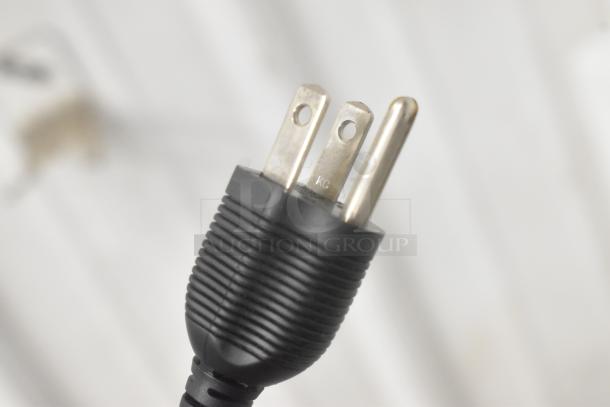 Close-up of a black AC power plug, showing a three-prong design with metal pins against a blurred background.