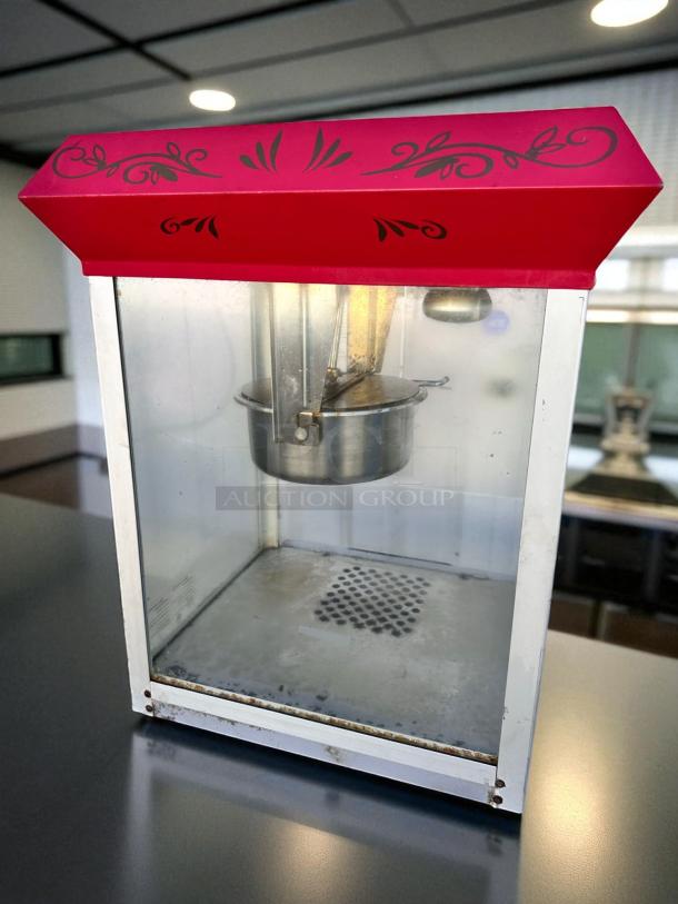 Vintage-style commercial popcorn machine in excellent condition, red top with black designs, fully tested and working.