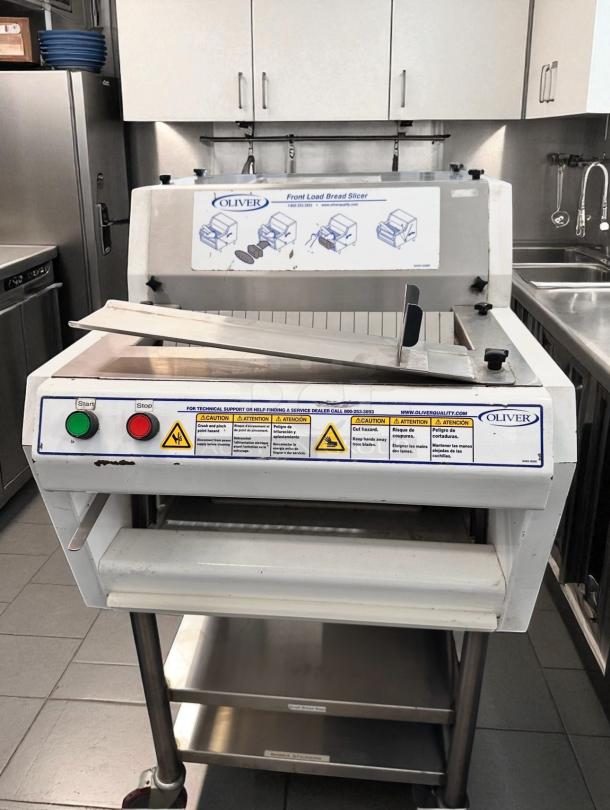 Oliver 702N front load bread slicer in excellent condition, fully tested, 115V. Features start/stop buttons and safety labels.