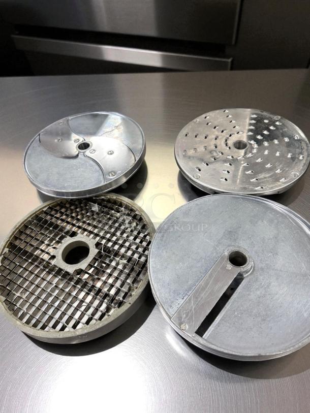 Robot Coupe CL50 Ultra food processor discs, various blade designs, clean condition, stainless steel countertop background.