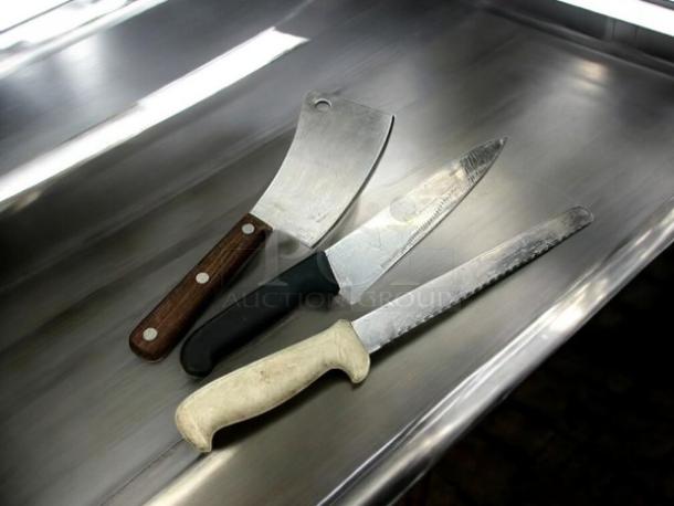 Three chef knives in great condition on stainless steel surface: a cleaver with wooden handle, a chef's knife with black handle, and a serrated knife with white handle.