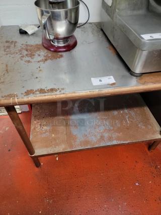 4-foot stainless steel work table with under-shelf. Signs of wear and rust. Ideal for commercial kitchen use.