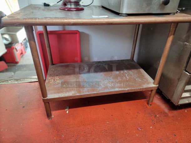 4-foot commercial stainless steel work table with lower shelf, used, showing wear and rust, ideal for kitchens or delis.