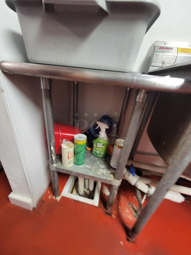 24" stainless steel work table with kitchen supplies, showing some visible wear. Includes cleaning items below. Buyer must remove.