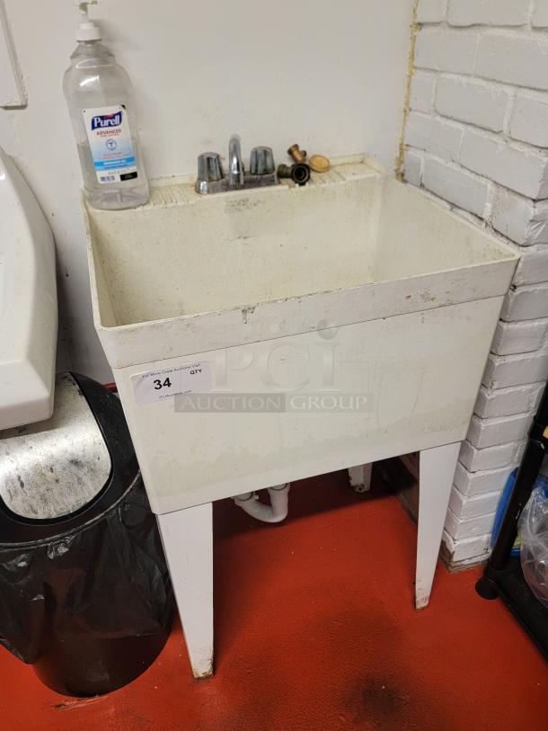White plastic utility sink with faucet and metal legs, in used condition. Includes soap dispenser and auction tag with item number 34.
