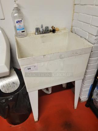 White plastic utility sink with faucet and metal legs, in used condition. Includes soap dispenser and auction tag with item number 34.