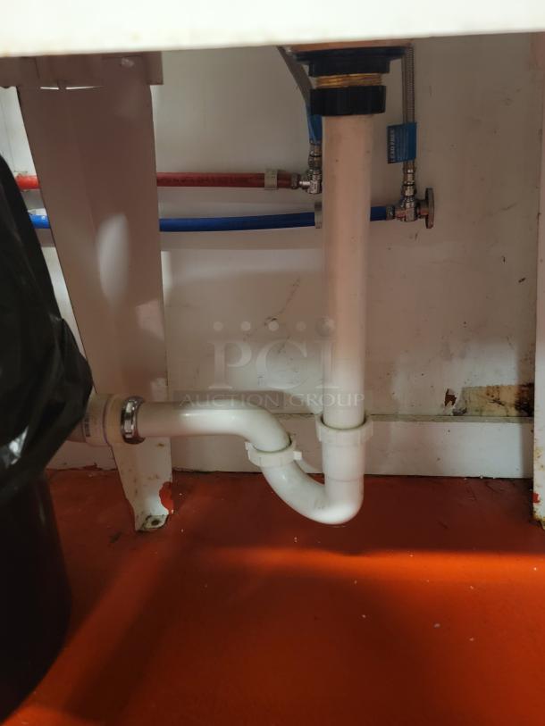 White plastic utility sink with faucet, metal legs, and visible plumbing pipes underneath. Ideal for commercial use. Buyer must remove.