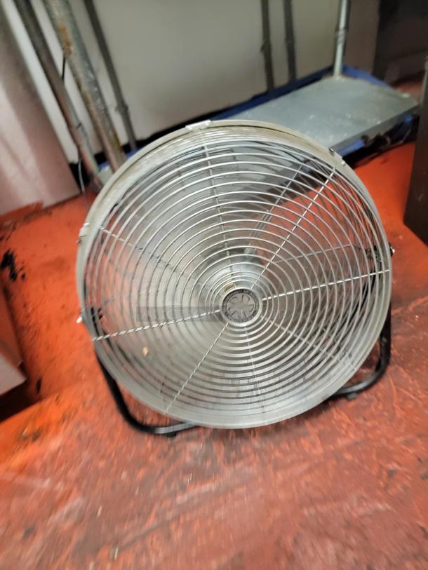 Industrial fan with metal protective grille and adjustable base. Ideal for air circulation in commercial spaces.