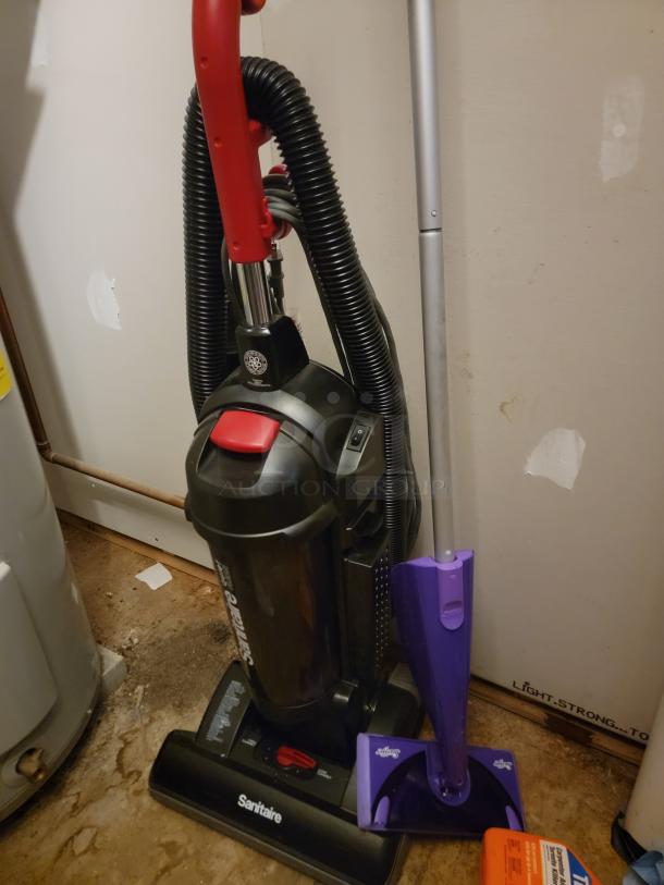 Sanitaire Quiet Clean commercial upright vacuum with red handle, black body, and logo visible on base. Purple mop in foreground.