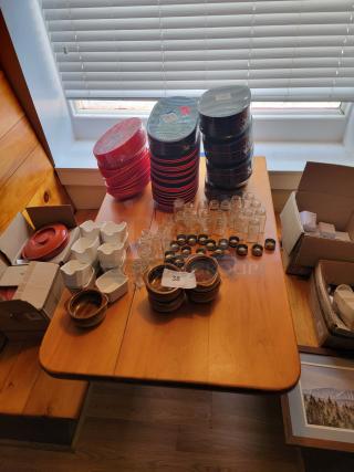 Huge lot of assorted commercial kitchen supplies on a wooden table, including plates, jars, bowls, and lids. Excellent condition.