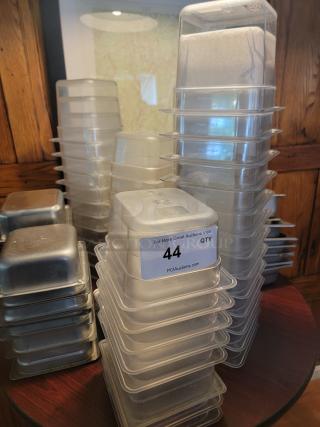 Assorted commercial food containers, including plastic and stainless steel, stacked, with label indicating auction lot number 44.