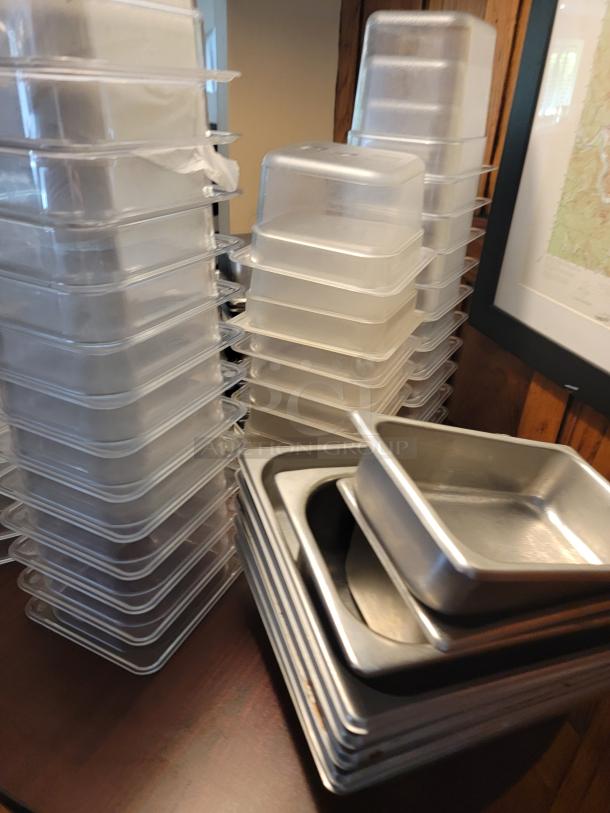 Assorted commercial food containers, plastic and stainless steel, stacked on a wooden table. Clean condition.