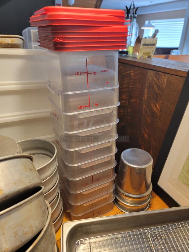 Assorted commercial food containers, including stacked clear plastic containers with red lids and stainless steel pans.