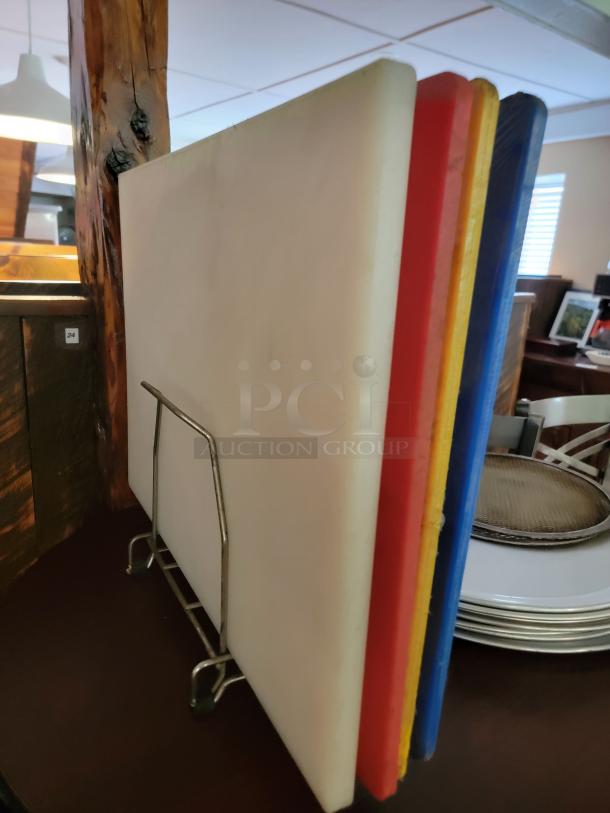 Multi-color commercial cutting boards on a metal rack, ideal for pizzerias. Visible perforated pizza pans in the background.