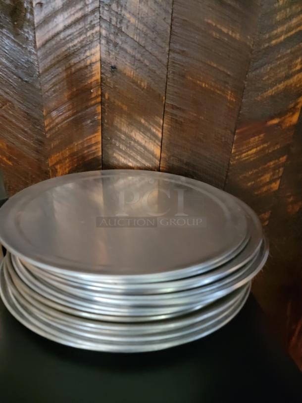 Stack of metal pizza pans, various sizes, suitable for commercial use. Ideal for pizzerias or home setups.