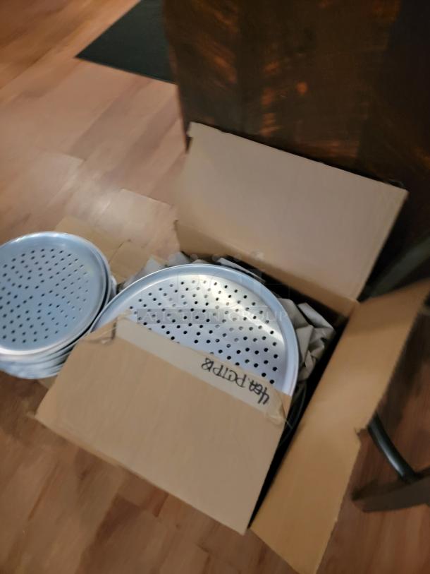 Box of perforated pizza pans for auction; essential for pizzerias. Marked box says "12A Perforated". Great for professional use.