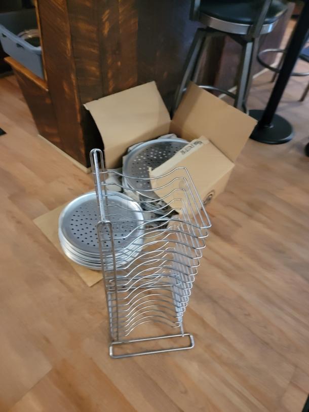 Commercial pizza equipment lot with perforated pans, pizza screens, and metal pan rack in good condition.