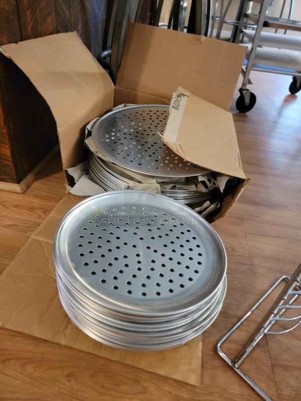 Stack of commercial perforated pizza pans in open cardboard box, Londonderry, VT. Ideal for pizzerias or food trucks.
