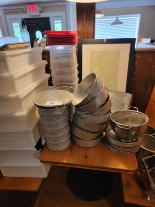 Assorted commercial aluminum cookware, storage bins, and wall art. Includes pans, colanders, and labeled food containers.