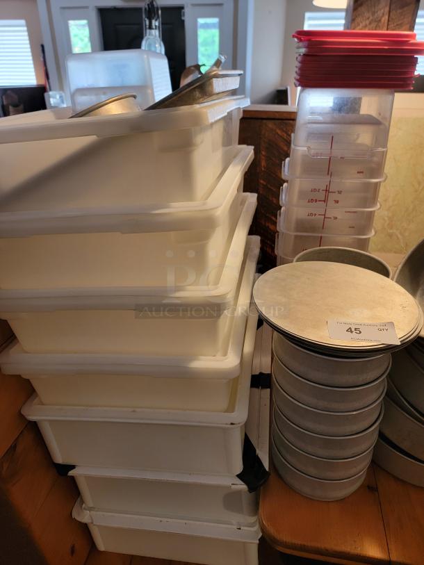Assorted commercial aluminum cookware stacked with white storage bins and lids, auction tag number 45 visible.