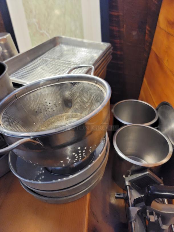 Assorted commercial aluminum cookware, including strainers and baking trays. Includes storage bins and wall art. Good condition.