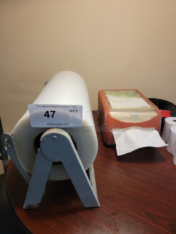 Roll of paper on metal dispenser, auction label "47" attached; napkin dispenser and small paper rolls beside it. Ideal for businesses.