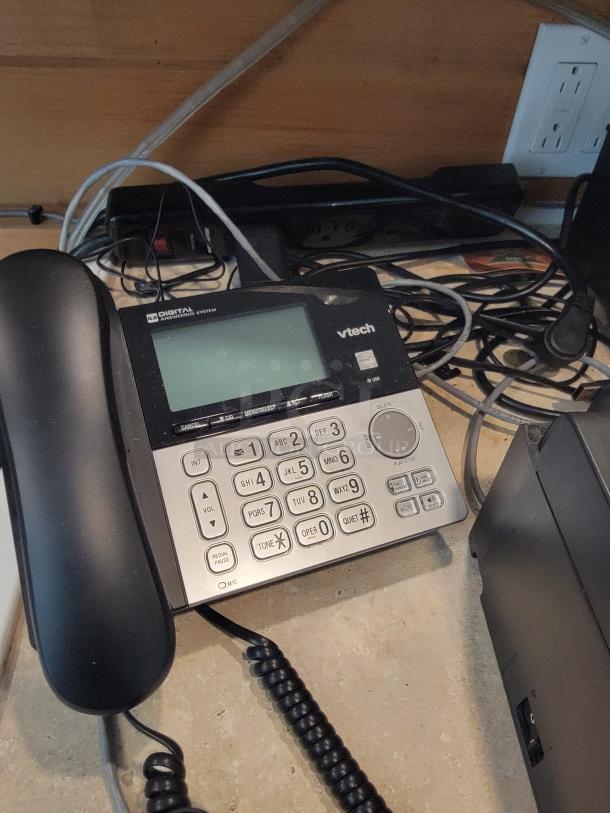 VTech digital answering system phone with keypad and display, shown in used condition, connected via cords.