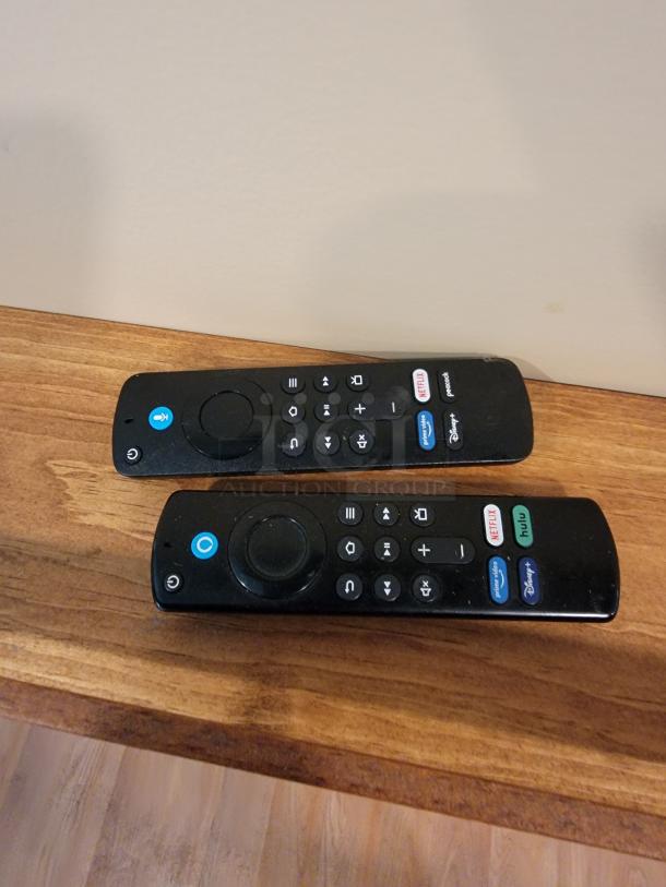 Two black TV remotes with Netflix, Hulu, Peacock, and Disney+ buttons on a wooden surface.