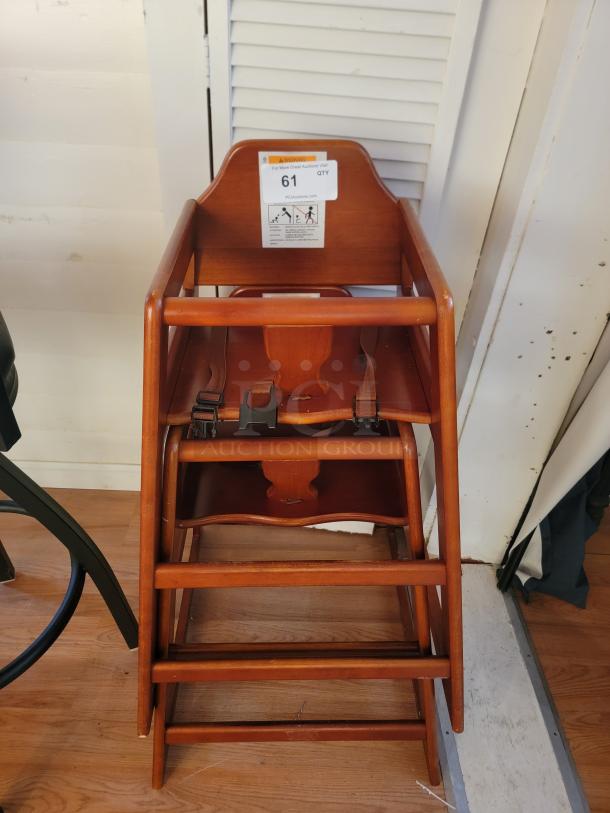 Sturdy wooden restaurant-style high chair with safety straps. Durable, easy to clean, ideal for cafes or home use. Auction label "61".