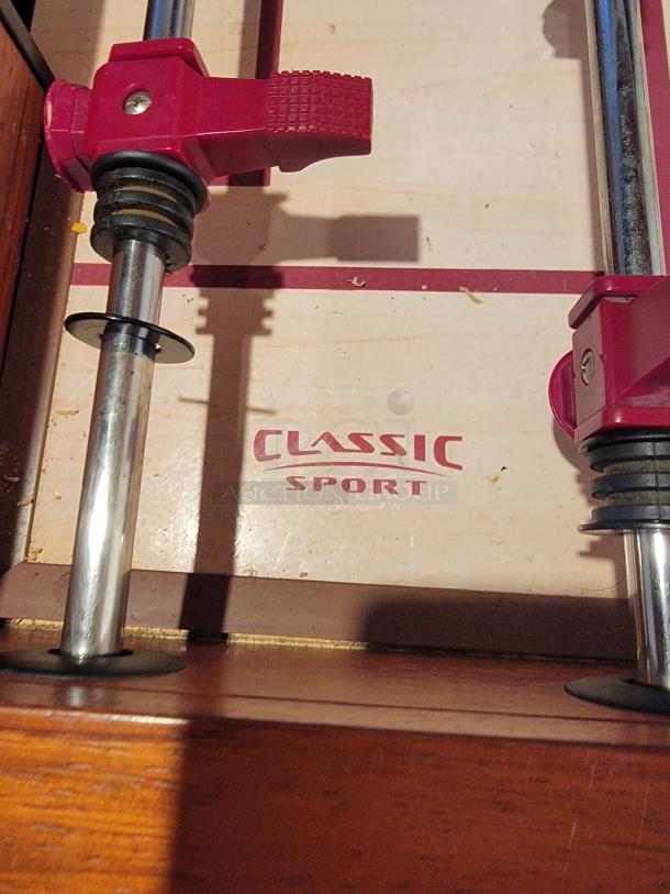 Classic Sport Foosball table with red player handles, chrome rods, and "Classic Sport" logo visible on the playing field.