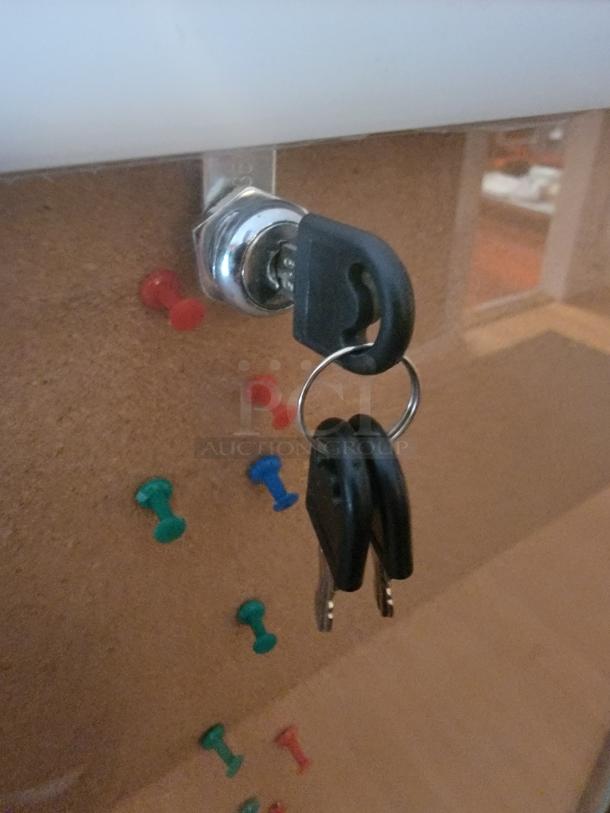 Enclosed cork bulletin board with lock, silver aluminum frame, includes keys. Condition appears excellent with visible push pins.