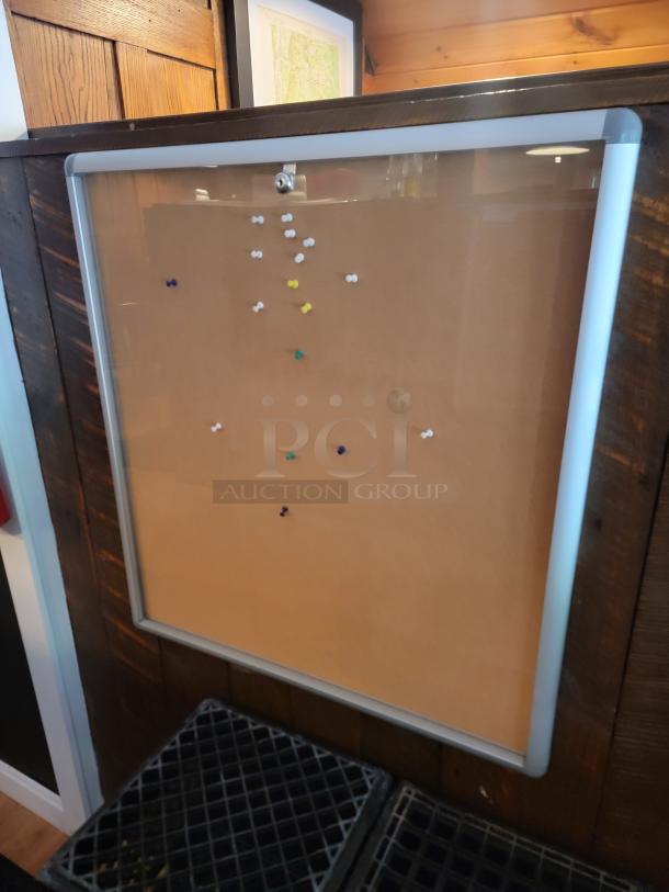 Enclosed cork bulletin board with lock, featuring a silver aluminum frame. Includes push pins; appears in good condition.