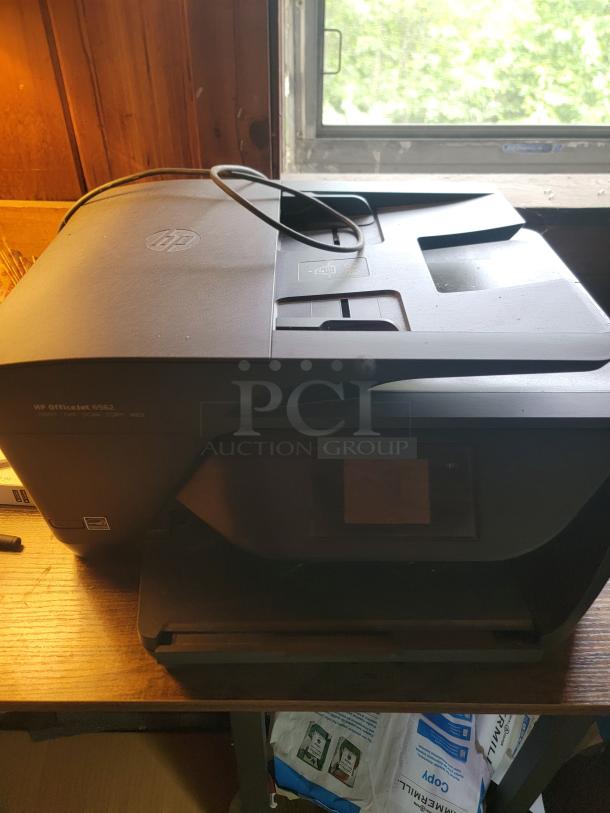 HP OfficeJet 6950 printer, black, on wooden desk. Features wireless printing. In used condition, power cord present.