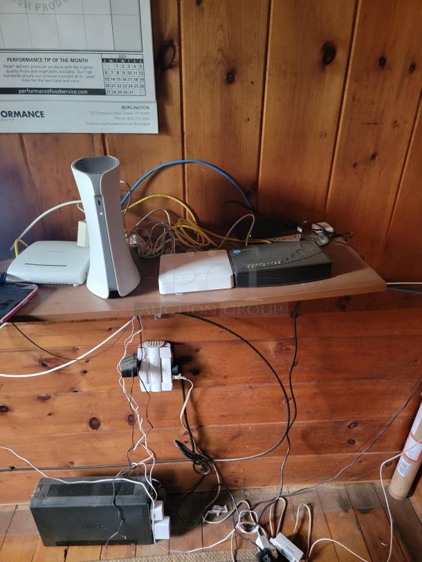Office equipment with routers, cables, and power strips on wooden shelf, set for auction. All items must be removed by buyer.