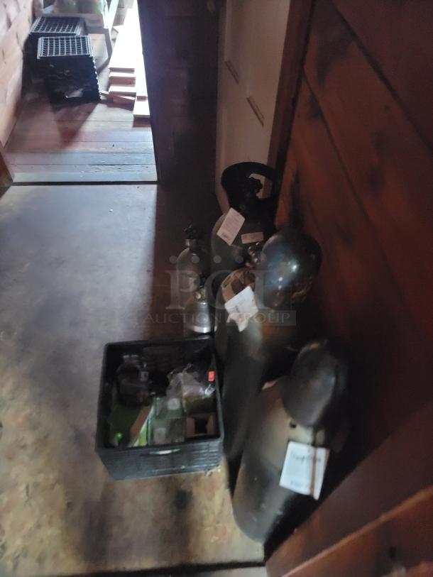 Assorted office items including gas cylinders with labels, a black crate with miscellaneous items, and stacks of wooden planks in a room.