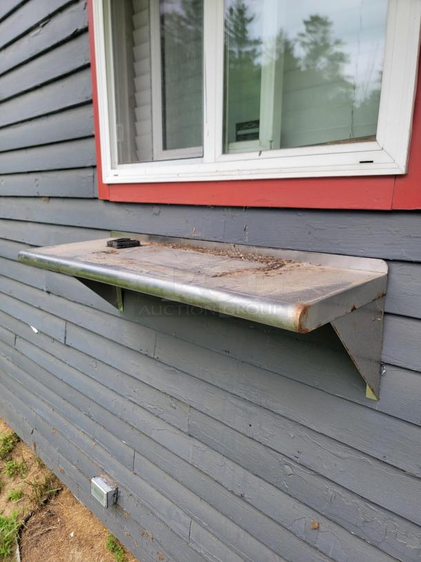 Profeeshaw stainless steel shelf mounted under a window, slightly weathered, ideal for professional spaces and easy to clean.