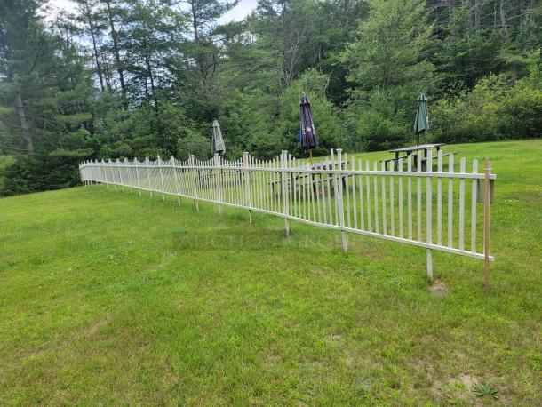 10 vinyl picket fence sections, each 4'x8', installed on grass. Classic design, ideal for gardens or property boundaries.