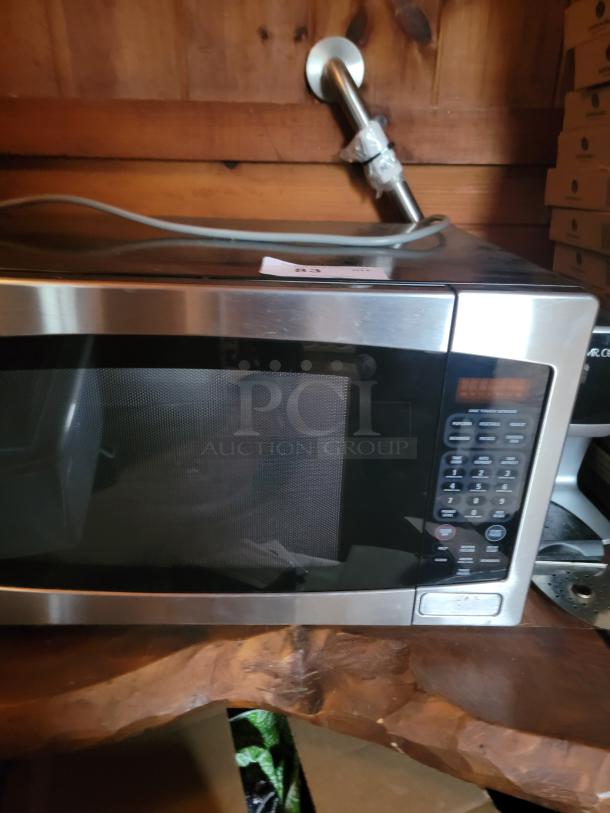 Stainless steel microwave oven, digital keypad, in good condition, placed on a wooden surface. Tag labeled "83".