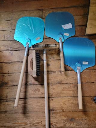 Brand new set of American Metalcraft pizza tools: 3 aluminum peels and 2 oven brushes with wooden handles on a wooden floor.
