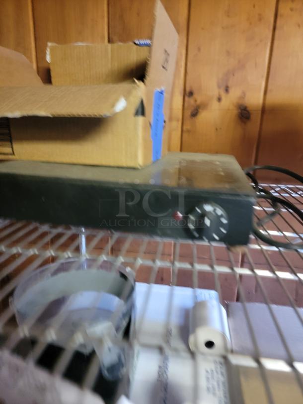 Commercial kitchen supply lot featuring chafing dishes, fry cutter, paper rolls, and more on wire shelving.